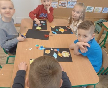 Na zdjęciu dzieci wykonują pracę plastyczną ,,Wirujące planety'.  - powiększ