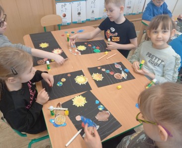 Na zdjęciu dzieci wykonują pracę plastyczną ,,Wirujące planety'.  - powiększ